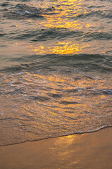 Sea wave foam on sandy beach in sundown light, close up. Tropical summery background.