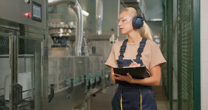 serious blonde attractive woman engineer concentrated on checking the industrial machine making notes in sheet of paper Scientist takes notes writes down observations in warehouse