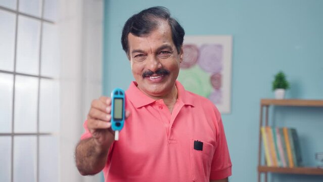 Happy Indian elderly senior man showing suger level checking glucometer by looking at camera - concept of Healthcare, happines and diabetes.