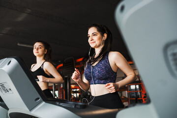 Two young pretty sports girls are training together on treadmills in a modern gym. Healthy and...