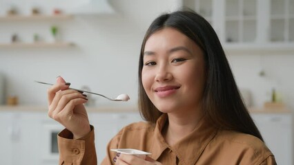 Asian korean woman girl tasting healthy nutrition eat creamy fruit yogurt in kitchen chinese girl smiling at camera eating dairy lactose dessert with spoon breakfast food loss weight diet healthcare - Powered by Adobe