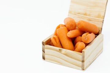 Wooden box with its lid open, full of fresh baby carrots isolated on a white background