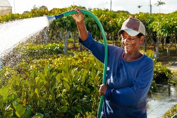 Black woman wearing a cap tending to a garden while watering the plants