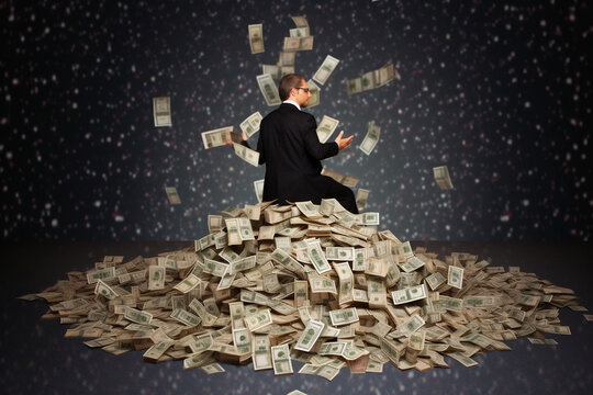 Suited White Business Man Sitting On A Large Pile Of Money While Trying To Control The Situation.