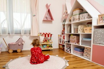 Happy young girl sits in a cozy playroom with a pink wall