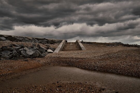 Concrete bridge rising above a sandy beach, with an overcast sky and dark clouds in the background.