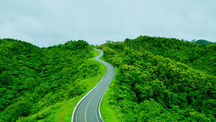 Aerial view of countryside road passing through the lush greenery and foliage tropical rain forest mountain landscape in Northern Thailand, Nan province. 