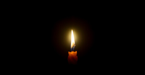 A single burning candle flame or light glowing on an orange candle on black or dark background on table in church for Christmas, funeral or memorial service with copy space