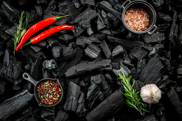 BBQ grill coal texture with fresh herbs, spices and kitchen utensils, cooking background, place for text, top view - obrazy, fototapety, plakaty