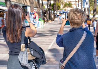 Two women of different ages together photographing city street life on a sunny day