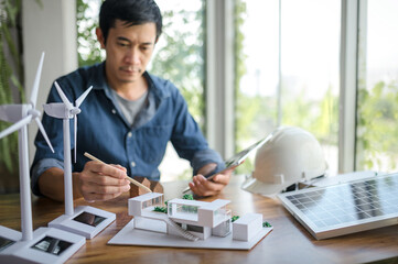 Selective focus on a pencil, Engineer sits holding tablet and looking at model of a house. with...