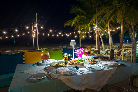 beach dinner table,Table set up for a romantic meal on the beach with lanterns and chairs and flowers with palm trees and sky and sea in the background.
