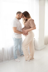 a man hugs a beautiful pregnant wife by the belly near a large window. family concept. pregnancy concept