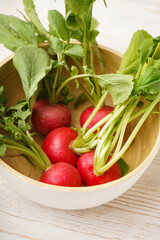 Ripe red radish in a bowl on a wooden background, close-up. Fresh red radish. Vertically.