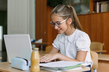smiling teenage girl in glasses working at laptop in classroom