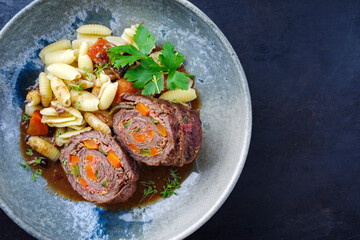 Traditionelle slow cooked deutsche Wagyu Rinderrouladen mit Gnocchetti-Sardi Nudeln in würziger Bratensoße als Draufsicht auf einem Nordic Design Teller mit Textfreiraum rechts