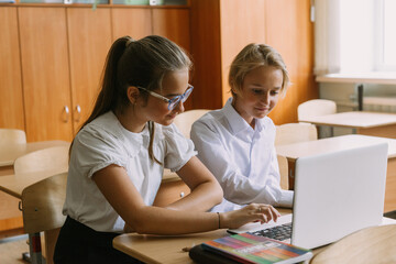 teen students working together writing in copybook using laptop in classroom