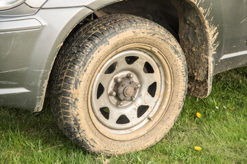Fototapeta na wymiar Car wheel tire covered in mud closeup on grassy meadow