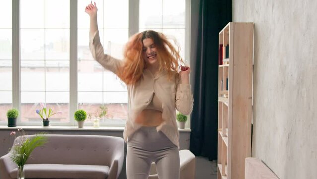 Moving shot female renter homeowner silly funky Caucasian woman in pajamas jump on bed happy free carefree girl having fun jumping dancing to music in bedroom home hotel weekend celebrating at morning