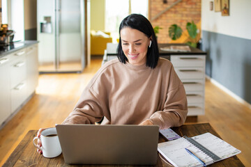 Young adult woman working on her laptop in the kitchen of her home