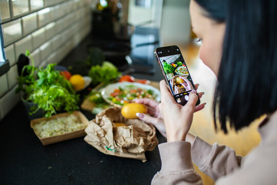 young adult woman taking a photo with her smart phone of a healthy salad she made at home