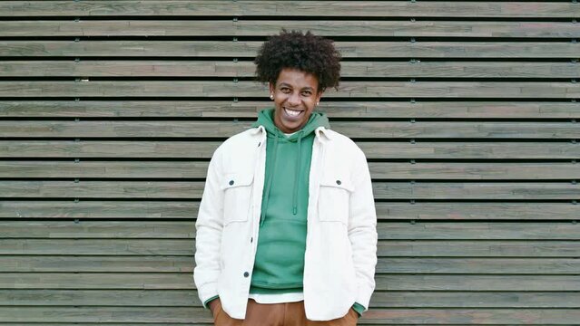 Young happy African American teen guy laughing on wooden wall background. Smiling cool ethnic generation z teenager student model standing looking at camera having fun, portrait outdoors.