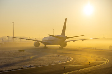 Fototapeta na wymiar Airplane taxing on taxiway in orange fog conditions. Yellow taxi line