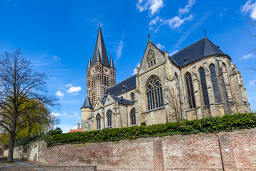 Fototapeta na wymiar Low angle perspective of Roman Catholic St. Michael Abbey church seen from the south against blue sky, bell tower with its clock and huge windows, sunny day in Thorn, Midden-Limburg in the Netherlands