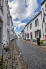 Urban landscape of a narrow cobbled street and sidewalks between buildings with white walls against blue sky and clouds, sunny day in old Dutch town of Thorn, Midden-Limburg in the Netherlands