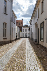 Fototapeta na wymiar Landscape of narrow cobbled street between house with white walls lantern and building in background against blue sky and clouds, gabled roofs, old Dutch town of Thorn in Midden-Limburg, Netherlands