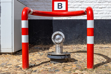 Fire hydrant between a red metal barrier with white lines against black and white wall, B for Brandweer, means: fire brigade, cobbled street in a Dutch village. Fire safety concept