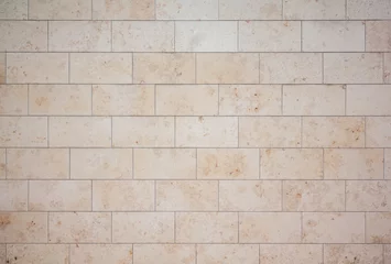Fotobehang texture of a tiled beige stone wall as background, natural stone wall texture as background. Close-up of a wall clad in limestone © Jarama