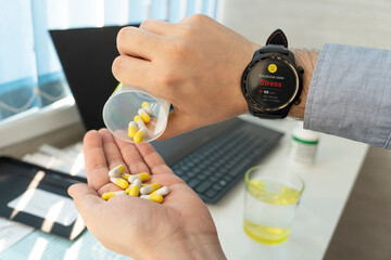 Obraz premium Sick mature man taking pills at work. stress and overwork at work concept. sick businessman drinks sedative pills. The smart watch shows emotional state on screen. Taking antidepressants at work.
