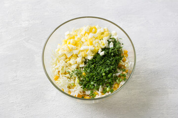 Glass bowl of white cabbage, sweet corn, egg, dill and green onion salad on a light gray background, top view. Stage of cooking healthy vegan salad