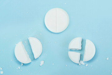 round tablet was divided equally. White pills on blue background. Few pills broken in half,...