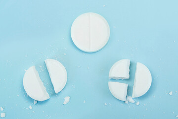 round tablet was divided equally. White pills on blue background. Few pills broken in half,...
