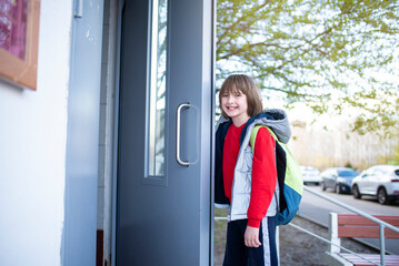 a boy opens the door to the entrance in spring, the child returns from school in spring alone