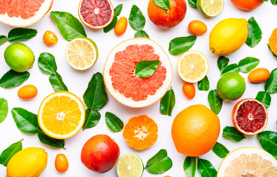 Citrus fruit food background, top view. Mix of different whole and sliced fruits: orange, grapefruit, lime and other with leaves on  white table