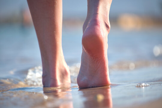 Close up of female feet walking barefoot on white grainy sand of golden beach on blue ocean water background