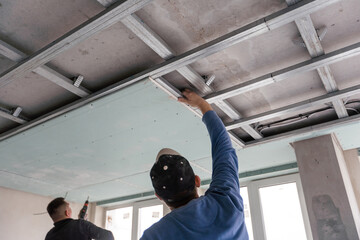 Workers fitting panel into frame of ceiling.
