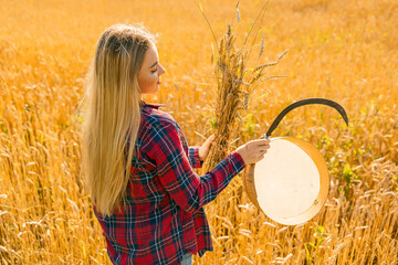 A peasant girl in a red shirt harvesting wheat with a sickle and an armful of wheat ears in her...