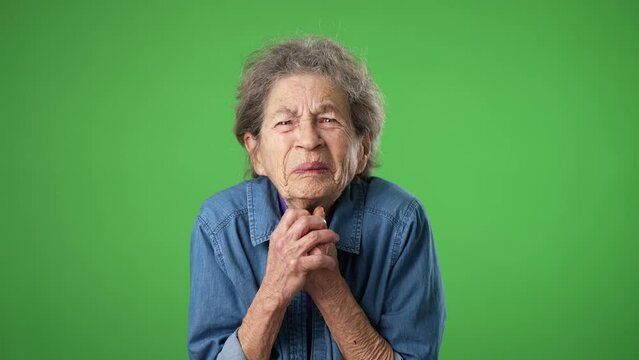 Portrait of tired, sleepy elderly senior old woman hold hands folded in prayer begging about something making wish keep fingers crossed isolated on green screen background studio.