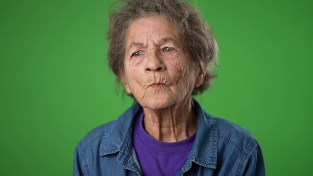 Funny slow motion closeup portrait of happy toothless elderly senior old woman with wrinkled skin and grey hair shrugging shoulders and gesturing I do not know isolated on green screen background.