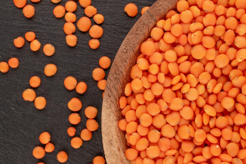 Red lentils on a wooden plate on a slate stone, macro, top view.