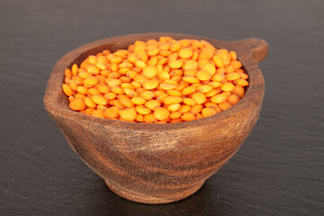 Red lentils in a wooden cup on a slate stone, macro.