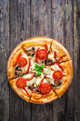 Circle vegetarian pizza with mozzarella cheese, mushrooms and tomatoes on wooden table
