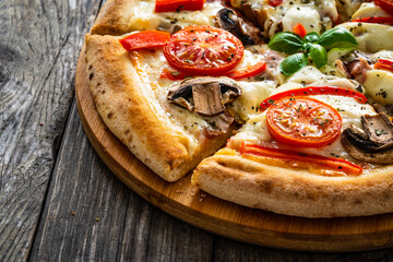 Circle vegetarian pizza with mozzarella cheese, mushrooms and tomatoes on wooden table
