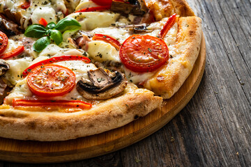 Circle vegetarian pizza with mozzarella cheese, mushrooms and tomatoes on wooden table

