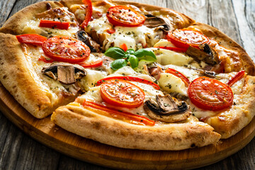 Circle vegetarian pizza with mozzarella cheese, mushrooms and tomatoes on wooden table
