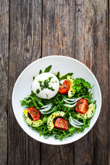 Burrata cheese with leafy greens, avocado and cherry tomatoes on wooden table
